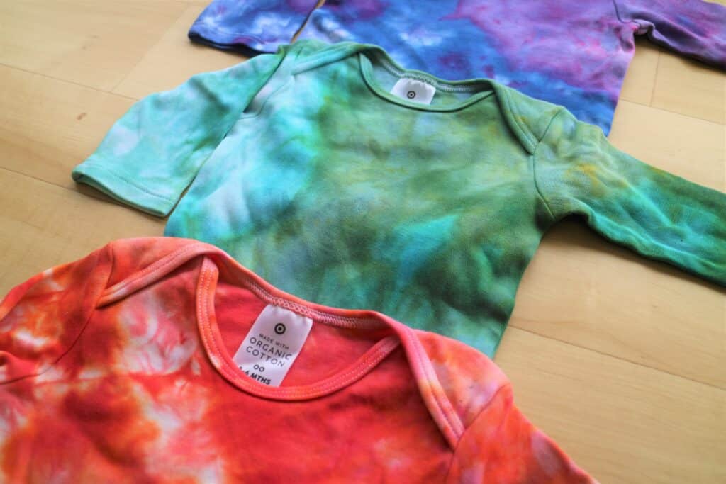 3 baby onesies, ice-dyed in a jar, green in centre, coral at bottom